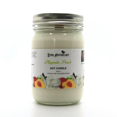 Photo of Byrd Apothecary Magnolia Peach Soy Candle with crackling Wooden Wick in a canning jar. The label background is a magnolia bloom and a cut open peach.